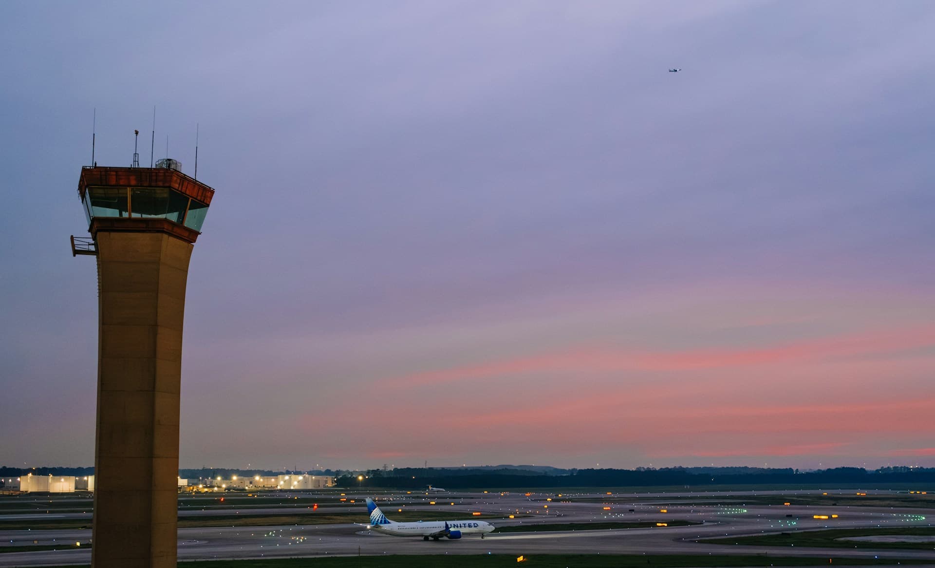 Air traffic control tower at twilight with aircraft and runway lights